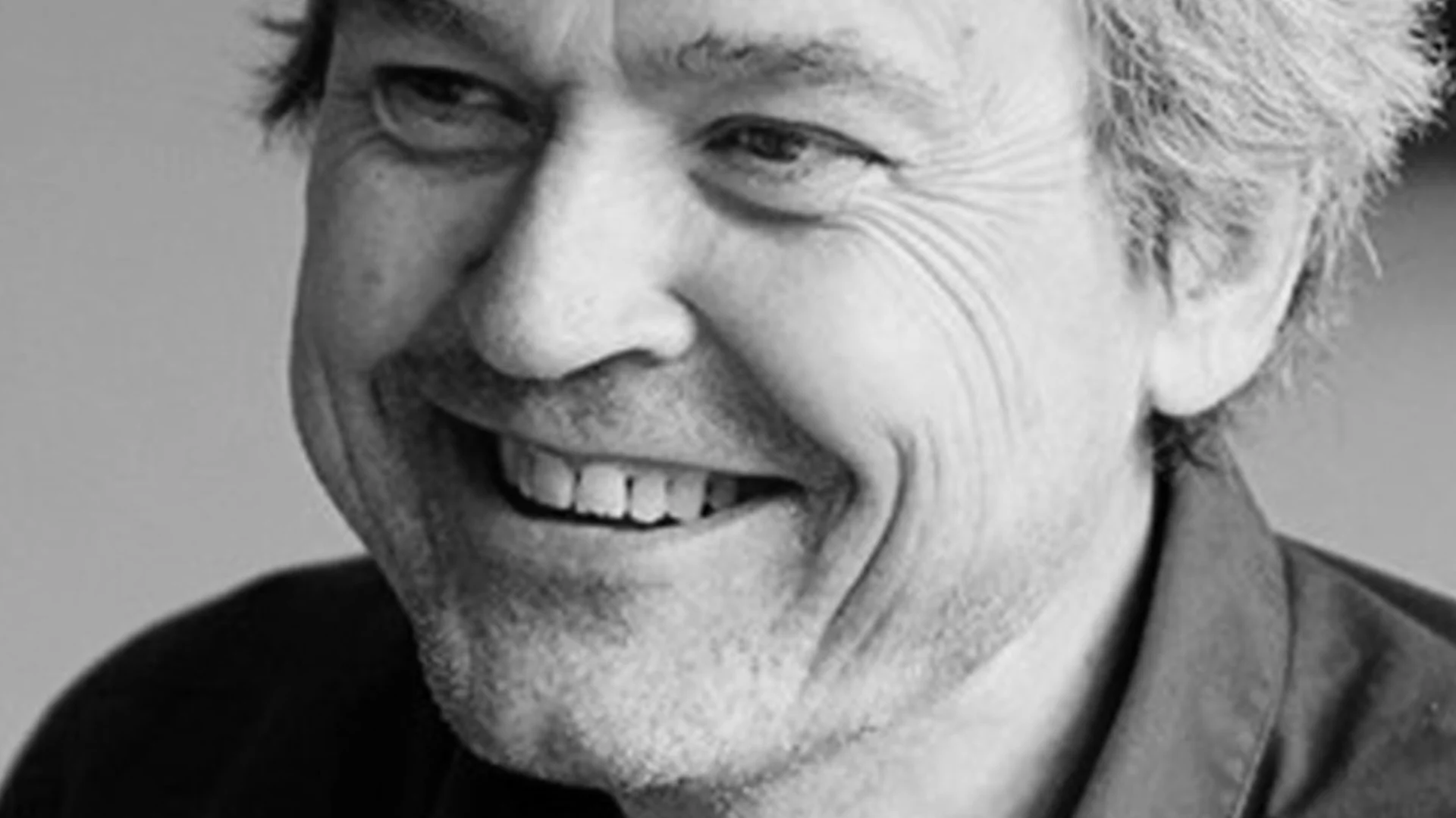Närbild i svartvitt av en leende man som tittar åt vänster.