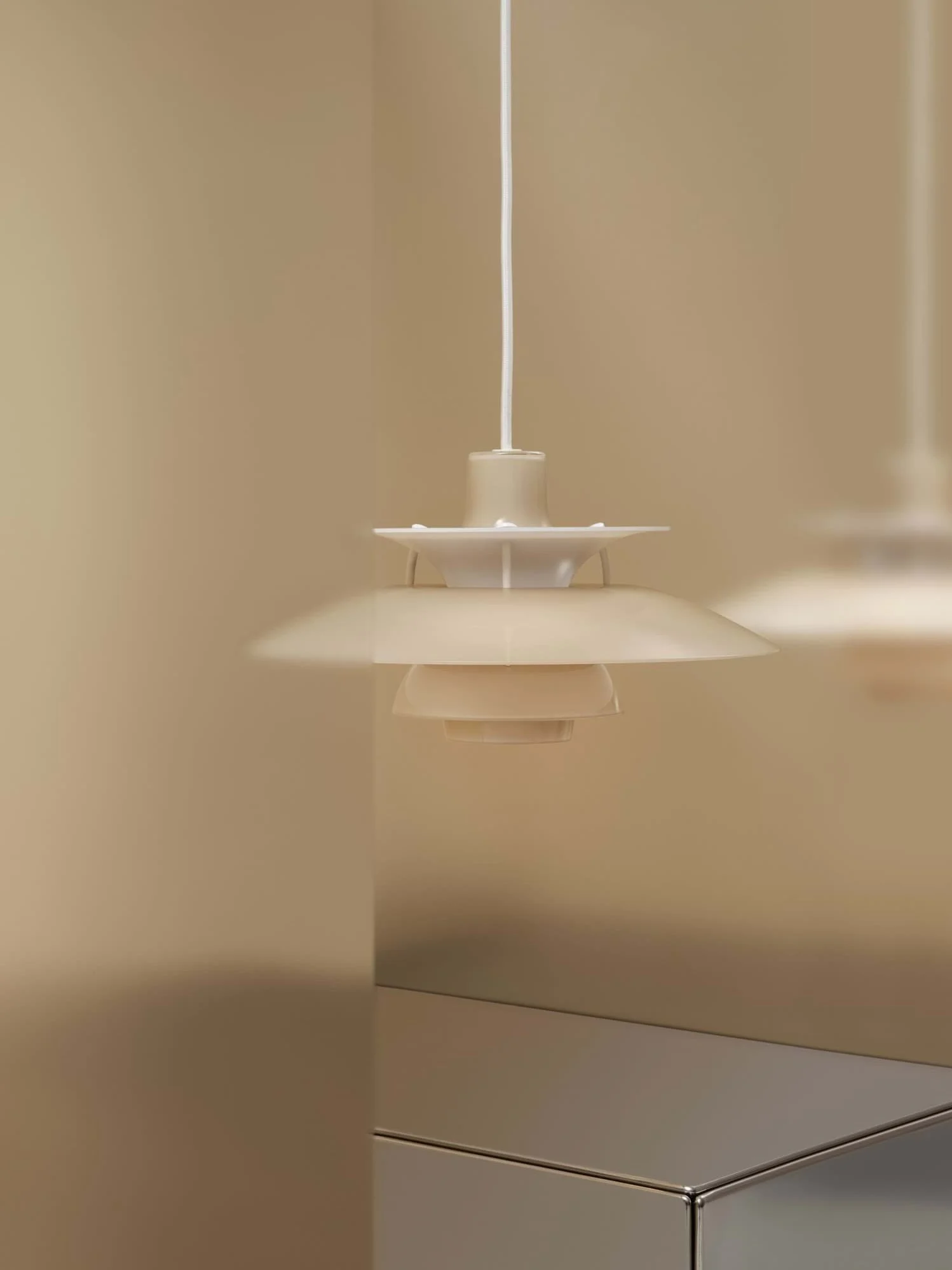 Beige flerskiktad taklampa hänger mot en beige vägg, med en reflekterande yta nedanför.