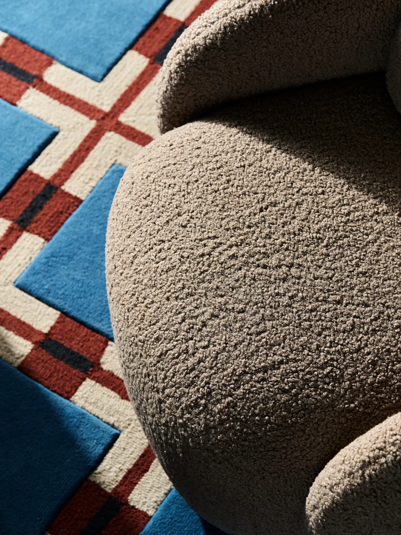 Närbild av en böjd, texturerad beige fåtölj på en geometriskt mönstrad matta.